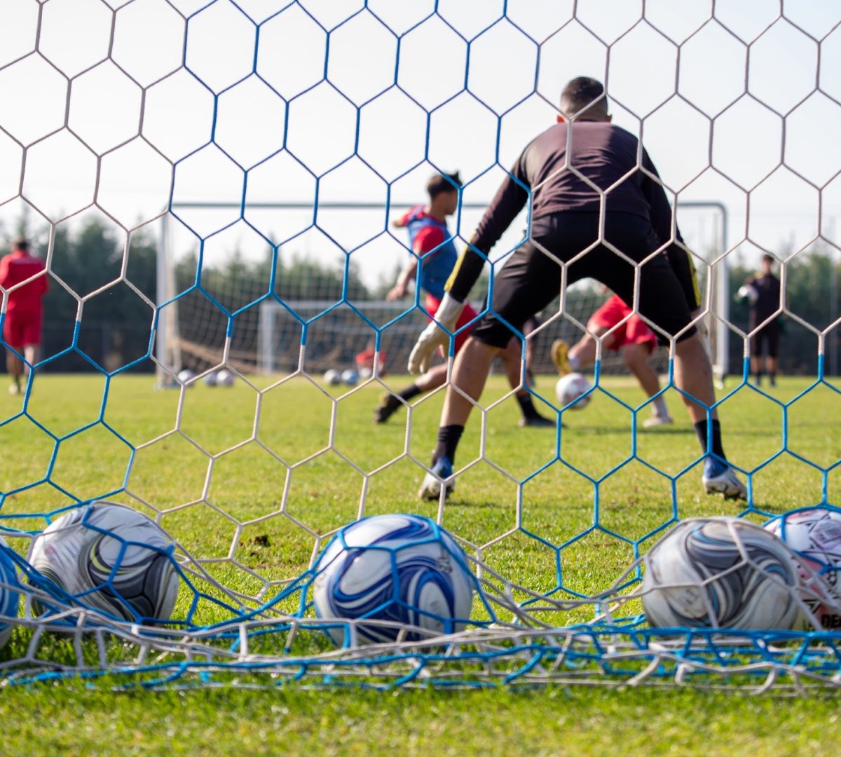 Soccer ball on field. Behind view of net, team training with football ball on grass background.